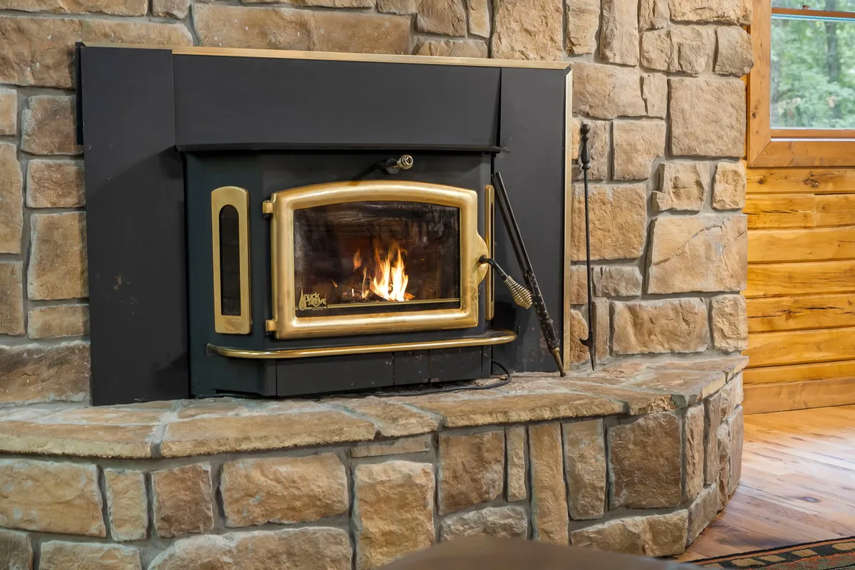 A warm, inviting interior featuring a rustic stone fireplace, wooden floors, and comfortable seating. The scene evokes cozy winter nights spent gathering around the fire, playing games, or sharing hot cocoa—core experiences described for the colder months at the cabin.