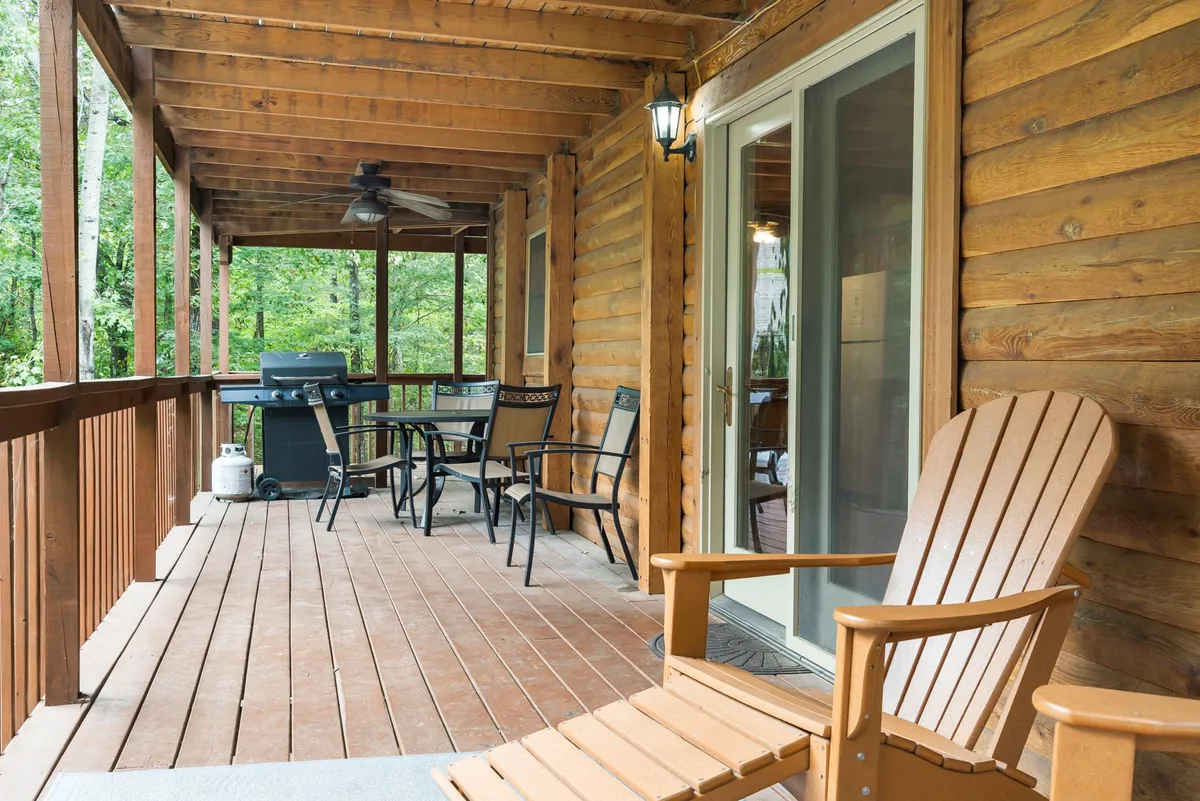 A wooden deck set for al fresco dining, featuring an Adirondack chair, an outdoor dining table with chairs, a gas grill for barbecues, and exterior lighting that makes the space inviting for evening meals and relaxation.