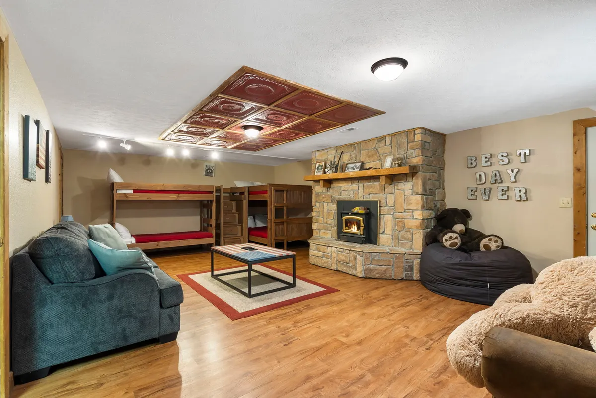 A cheerful bunkroom with two sets of bunk beds, a stone fireplace, comfortable seating, and a wall displaying 'BEST DAY EVER.' The room is designed for group fun as well as restful nights, with playful touches perfect for kids or extra guests.