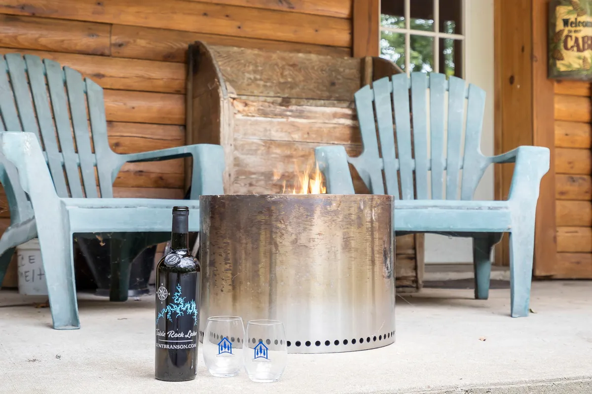 An inviting outdoor fire pit area encircled by Adirondack chairs, with a bottle of wine and glasses set out, creating a warm ambiance for evening gatherings and storytelling under the stars.
