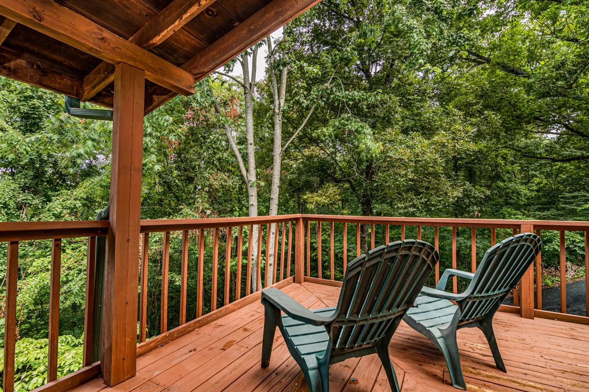 A spacious wooden deck furnished with vibrant green chairs overlooks a backdrop of dense, leafy foliage. The setting is tranquil, inviting relaxation and providing an open, easily accessible connection to the outdoors—an ideal spot for guests to unwind while keeping an eye on their pets as they play nearby.