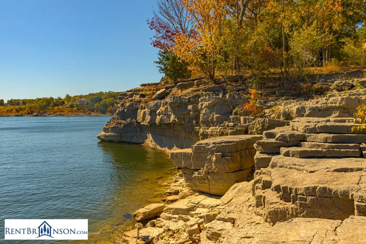 A breathtaking exterior landscape featuring unique rock formations, calm water reflecting autumn foliage, and a peaceful ambiance. The scene invites outdoor activities such as hiking, fishing, photography, or simply enjoying the sunset over the water.