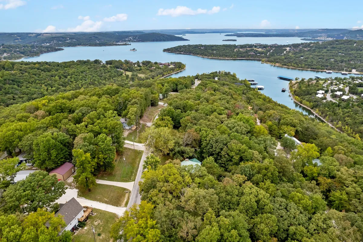 A panoramic view of a scenic lake fringed by vibrant green trees, with winding roads meandering through the forested landscape. The scene is peaceful, offering a sense of expansive outdoor possibilities including hiking, boating, and wildlife watching.