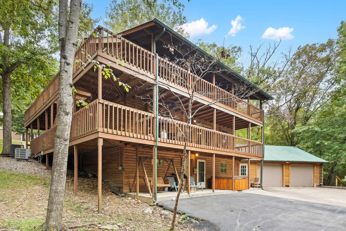 A welcoming exterior view of the three-story wooden cabin, complete with expansive balconies and an outdoor seating area surrounded by nature. The scene evokes a sense of togetherness, as guests can be seen relaxing and socializing outdoors.