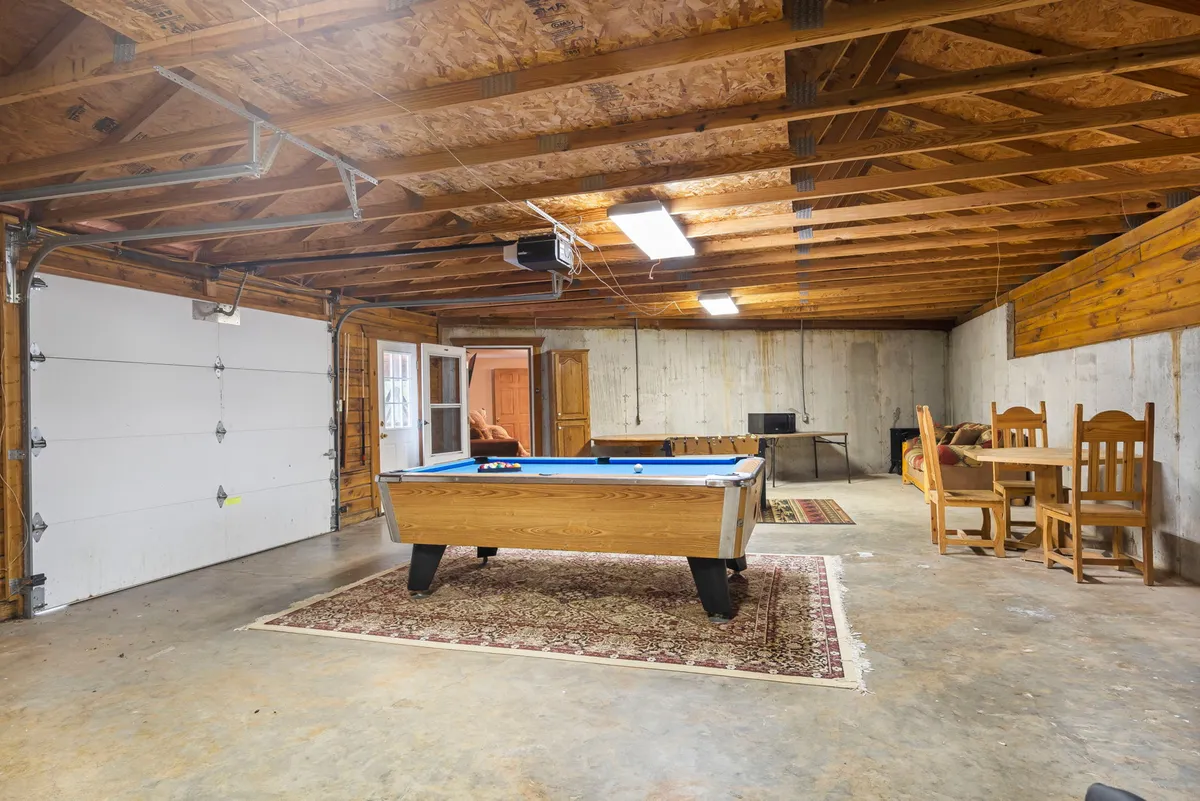This image presents another view of the game room, focusing on a pool table, a dining table for gatherings, and the garage door open to let in natural light. People are seen socializing, which reinforces the area's role as a lively family and friends hub.